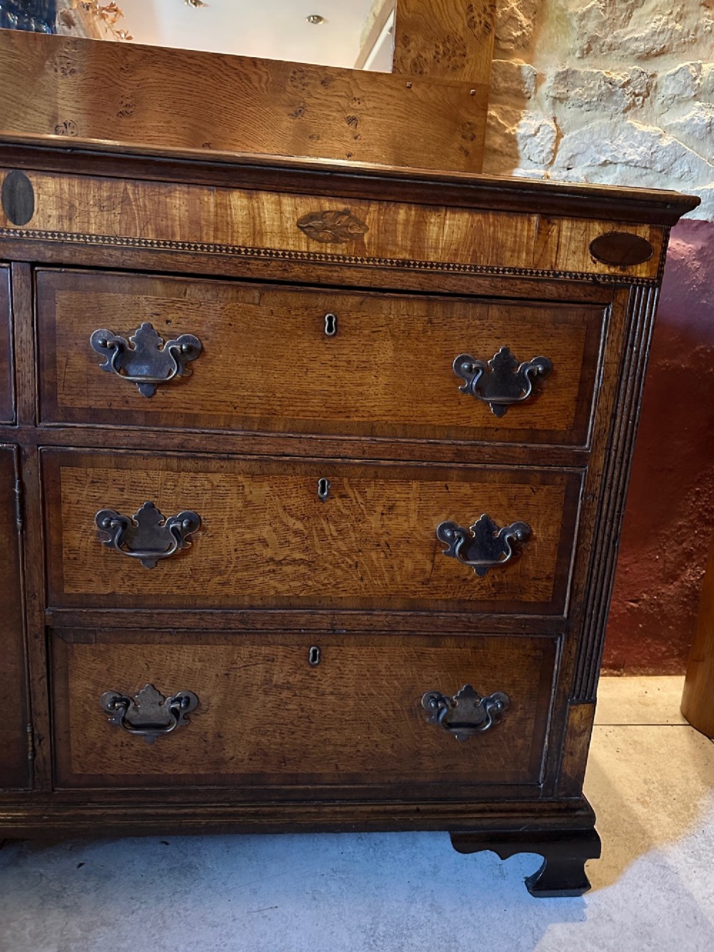 A Georgian oak Lancashire dresser base circa 1800 featuring drawer configuration, central cupboard doors with oval mahogany inlays, and brass handles. View V