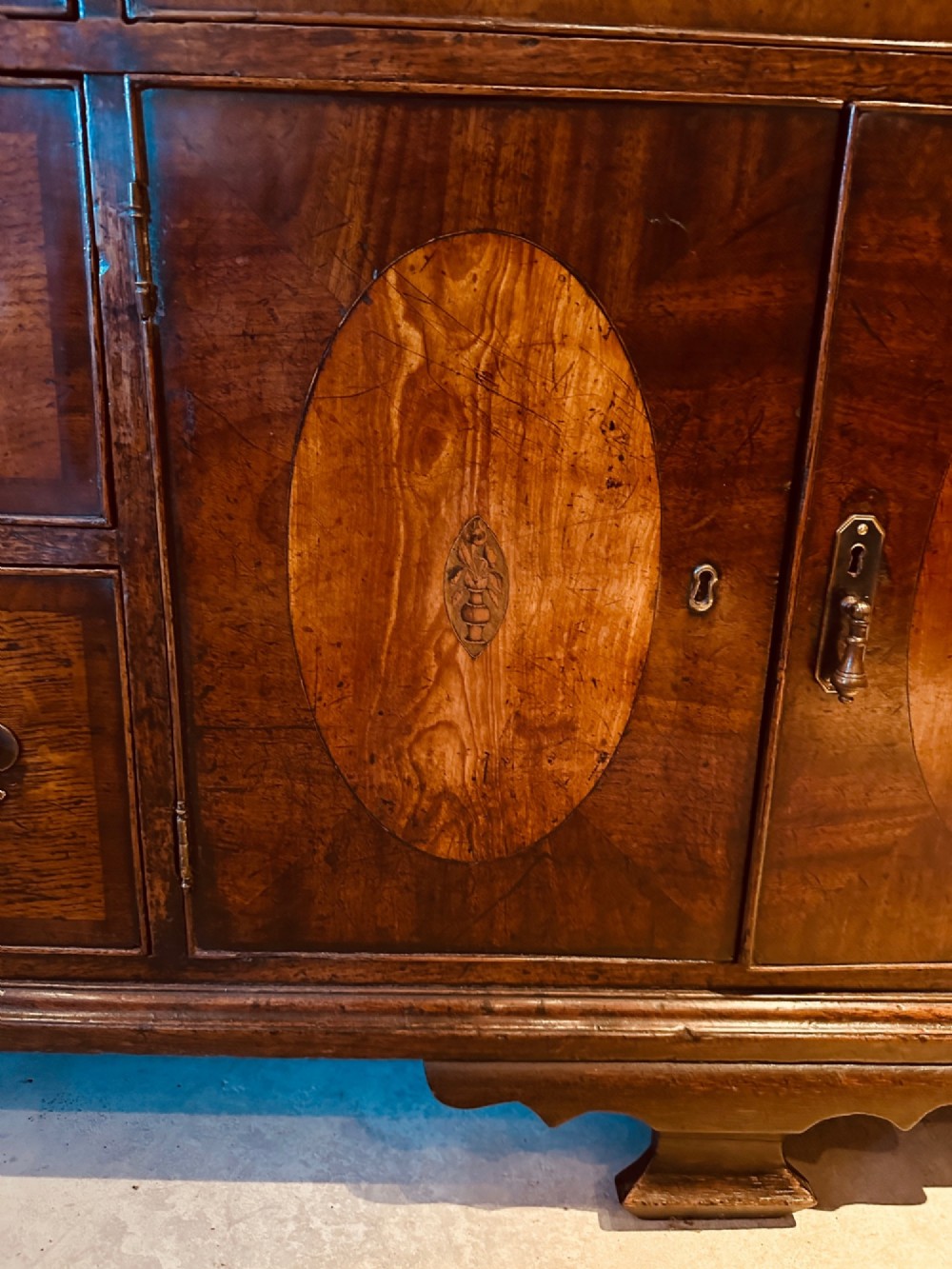 A Georgian oak Lancashire dresser base circa 1800 featuring drawer configuration, central cupboard doors with oval mahogany inlays, and brass handles. View VI
