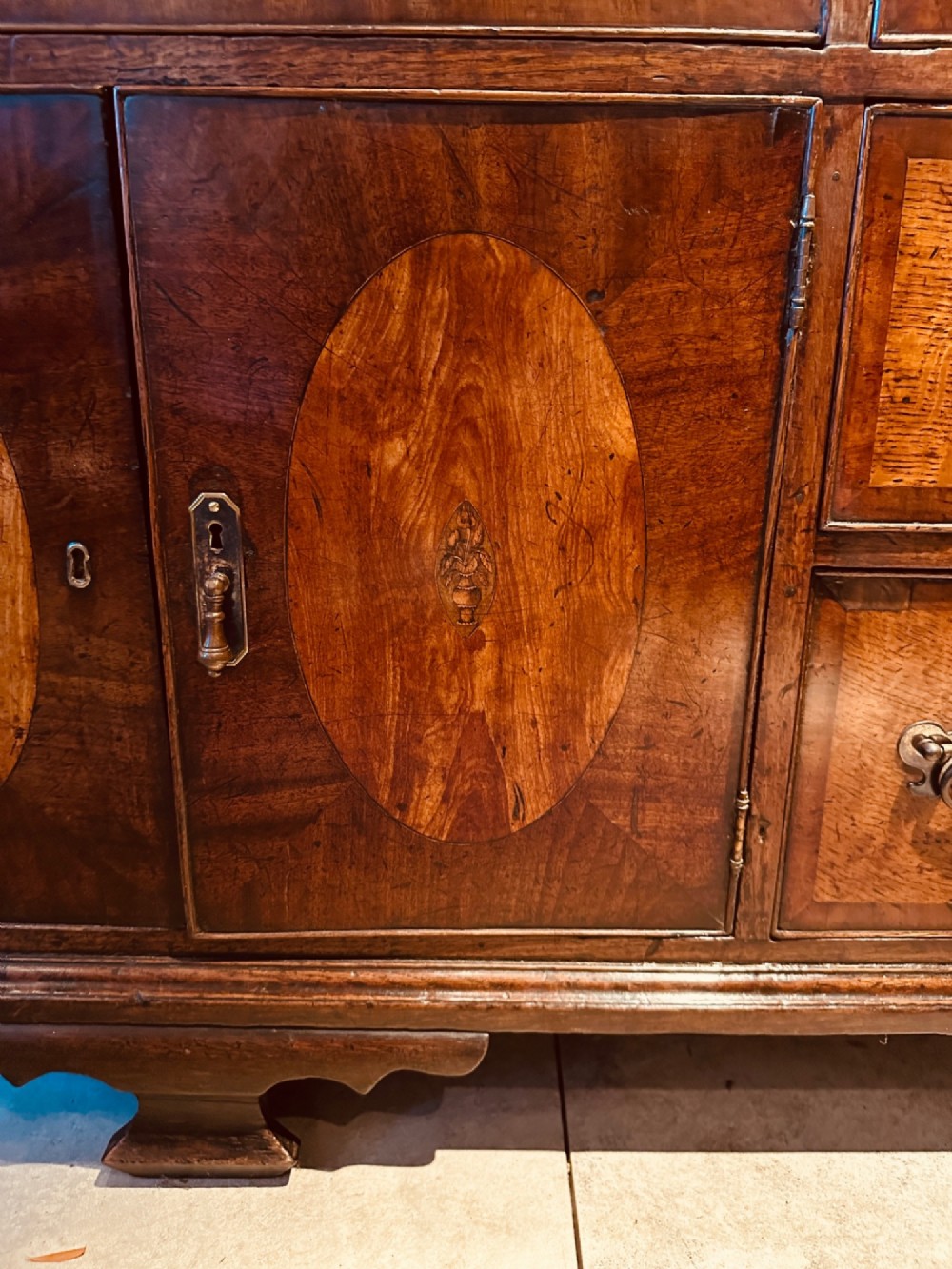 A Georgian oak Lancashire dresser base circa 1800 featuring drawer configuration, central cupboard doors with oval mahogany inlays, and brass handles. View VII