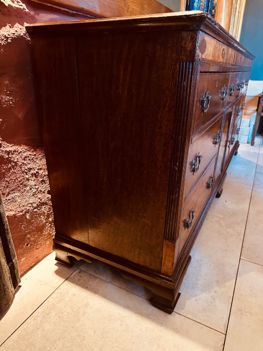 A Georgian oak Lancashire dresser base circa 1800 featuring drawer configuration, central cupboard doors with oval mahogany inlays, and brass handles. View IX
