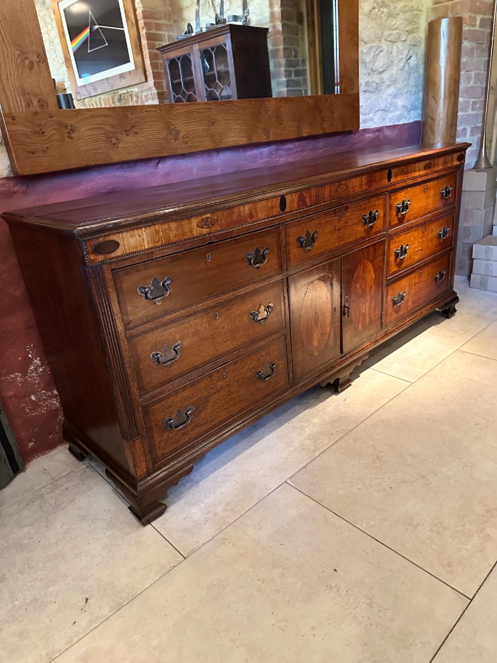 A Georgian oak Lancashire dresser base circa 1800 featuring drawer configuration, central cupboard doors with oval mahogany inlays, and brass handles. View X