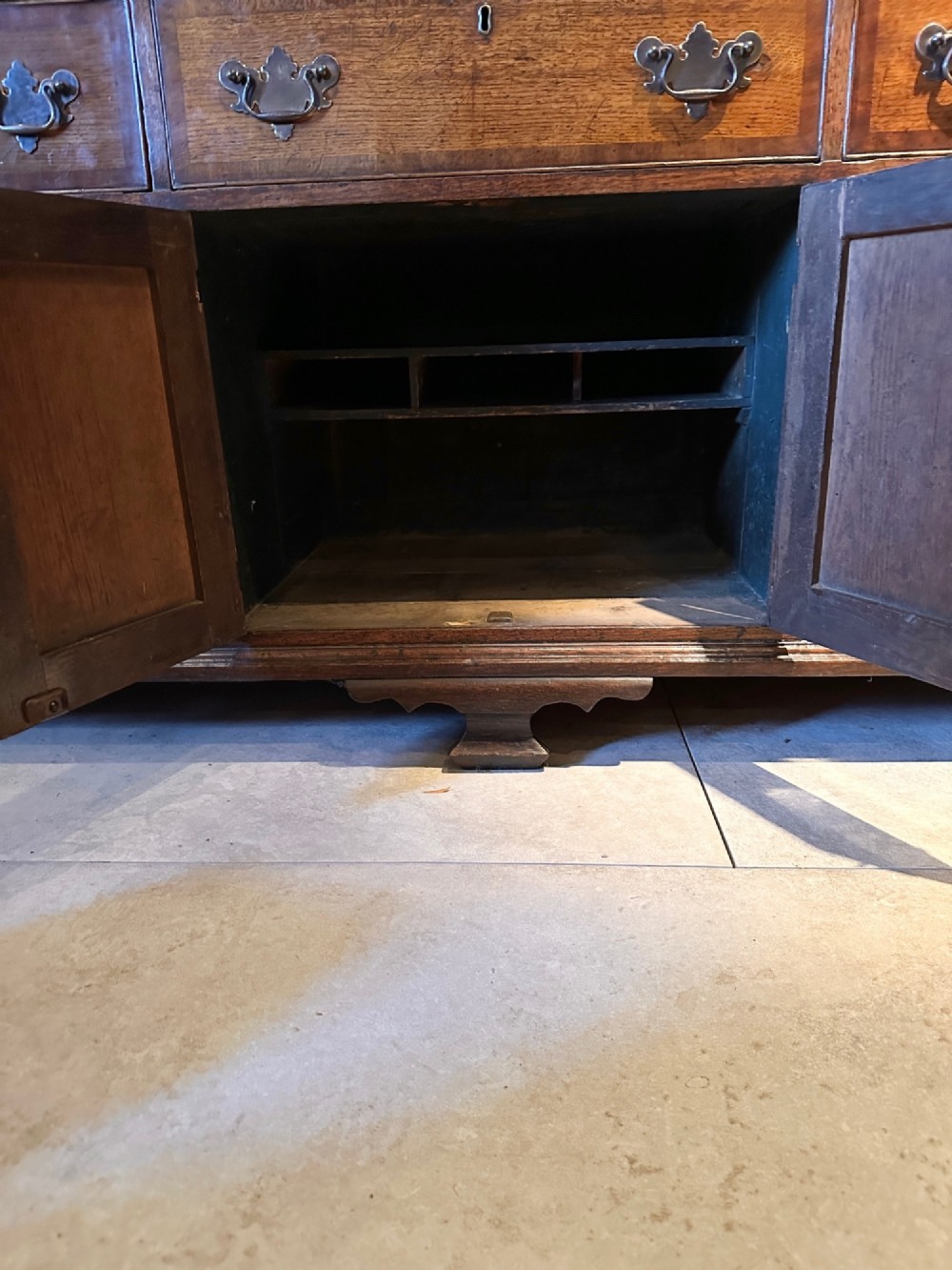 A Georgian oak Lancashire dresser base circa 1800 featuring drawer configuration, central cupboard doors with oval mahogany inlays, and brass handles. View XII