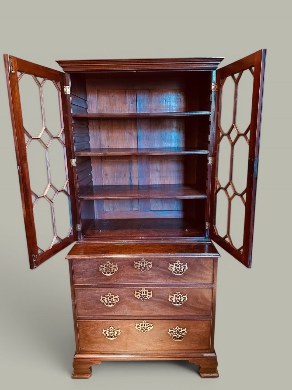 An antique mahogany bookcase on chest featuring a two-door astragal glazed upper display section and three long drawers with decorative brass handles below. View II