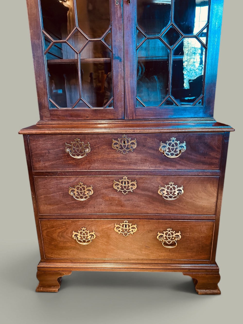 An antique mahogany bookcase on chest featuring a two-door astragal glazed upper display section and three long drawers with decorative brass handles below. View III