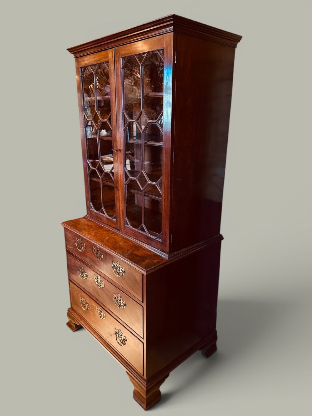 An antique mahogany bookcase on chest featuring a two-door astragal glazed upper display section and three long drawers with decorative brass handles below. View IV