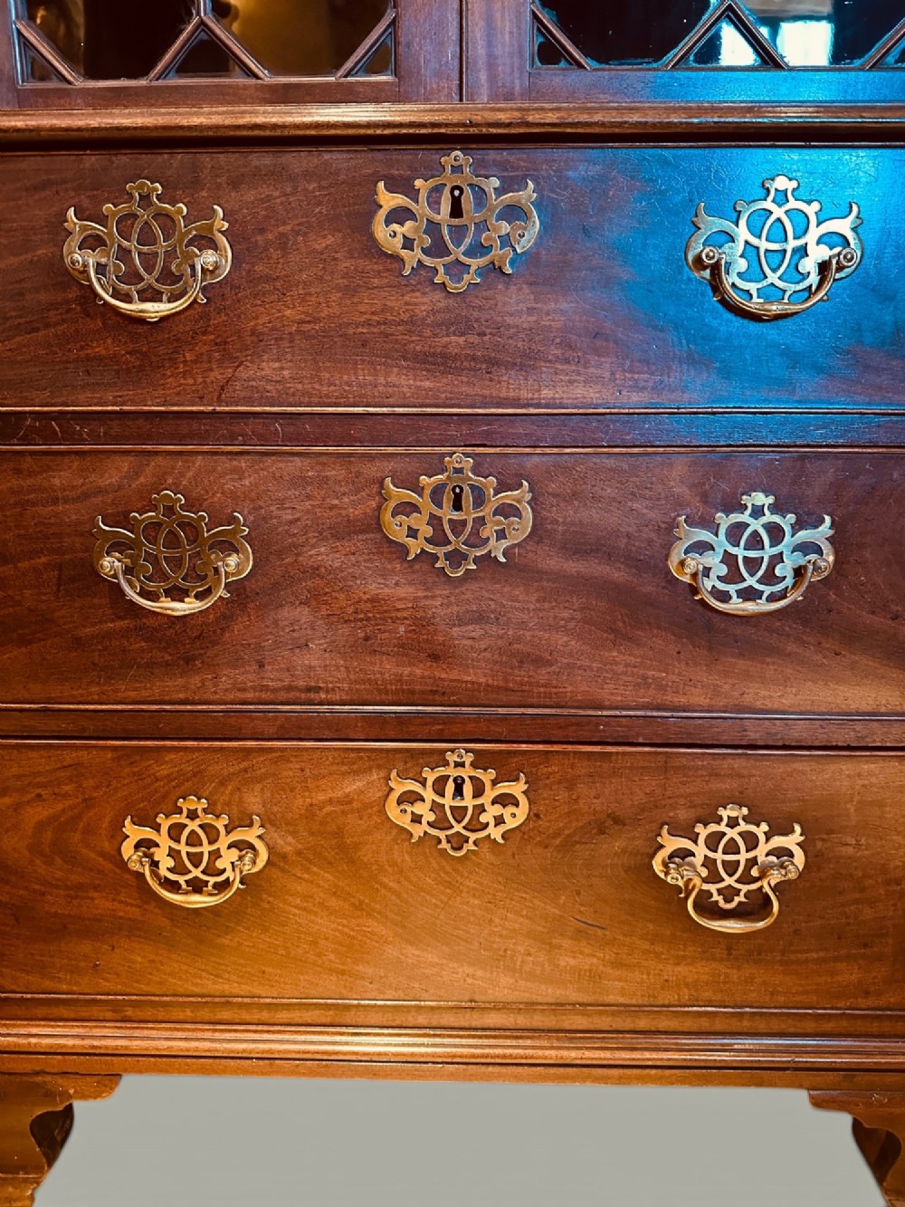 An antique mahogany bookcase on chest featuring a two-door astragal glazed upper display section and three long drawers with decorative brass handles below. View V