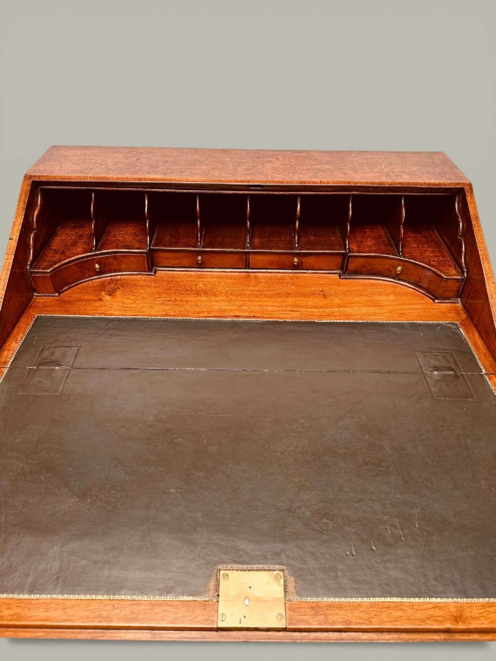 An antique Georgian kneehole bureau in warm brown burr oak featuring multiple small drawers, brass drop handles, a central cupboard, and a hinged top surface. View III