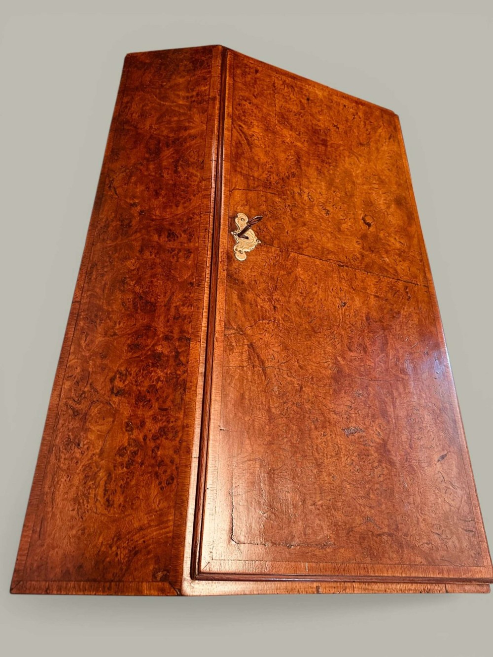 An antique Georgian kneehole bureau in warm brown burr oak featuring multiple small drawers, brass drop handles, a central cupboard, and a hinged top surface. View V