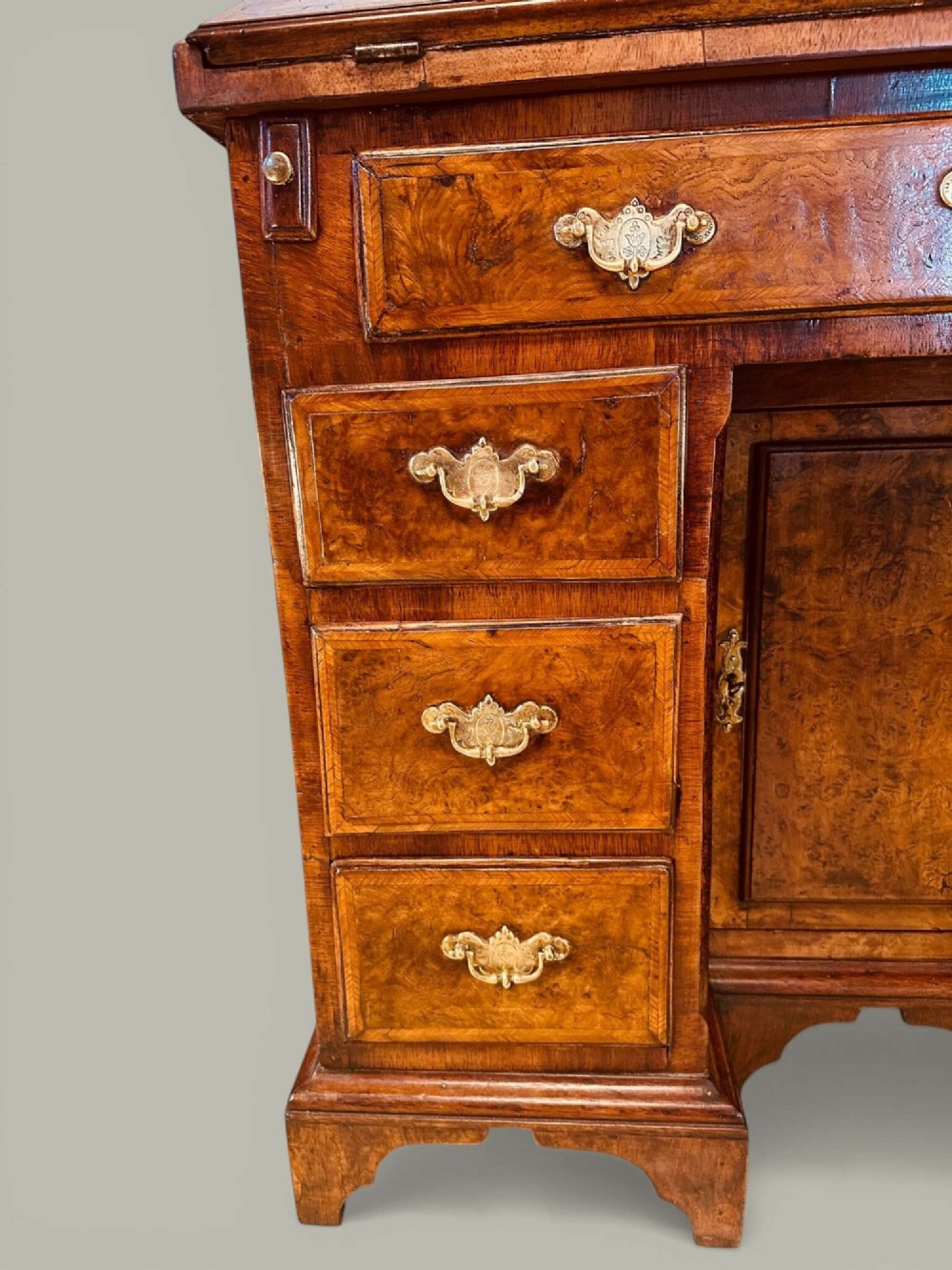 An antique Georgian kneehole bureau in warm brown burr oak featuring multiple small drawers, brass drop handles, a central cupboard, and a hinged top surface. View VII
