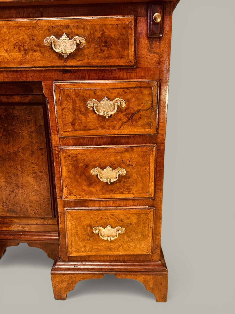 An antique Georgian kneehole bureau in warm brown burr oak featuring multiple small drawers, brass drop handles, a central cupboard, and a hinged top surface. View VIII
