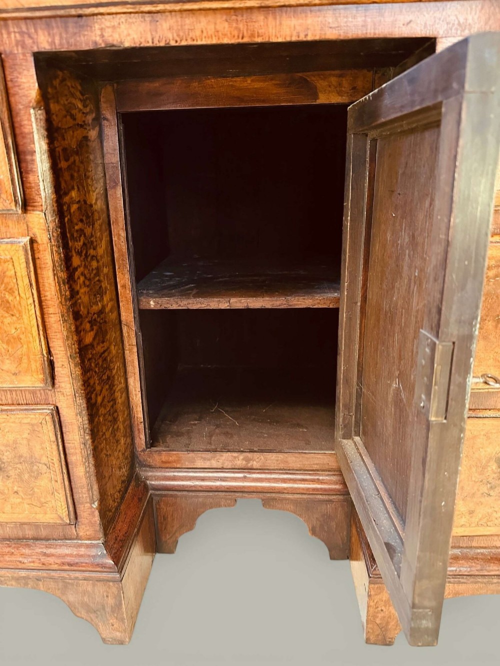 An antique Georgian kneehole bureau in warm brown burr oak featuring multiple small drawers, brass drop handles, a central cupboard, and a hinged top surface. View IX