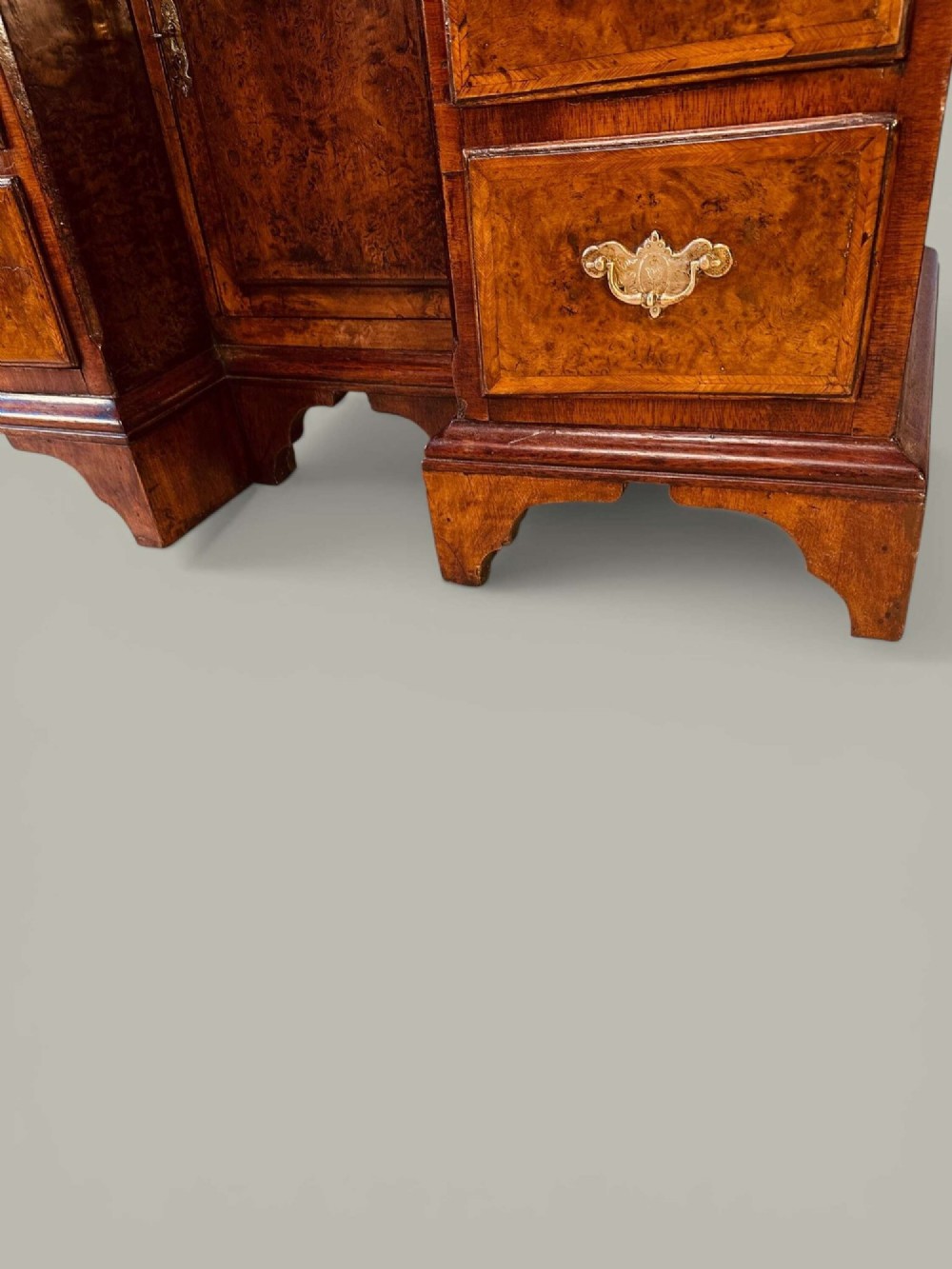 An antique Georgian kneehole bureau in warm brown burr oak featuring multiple small drawers, brass drop handles, a central cupboard, and a hinged top surface. View X