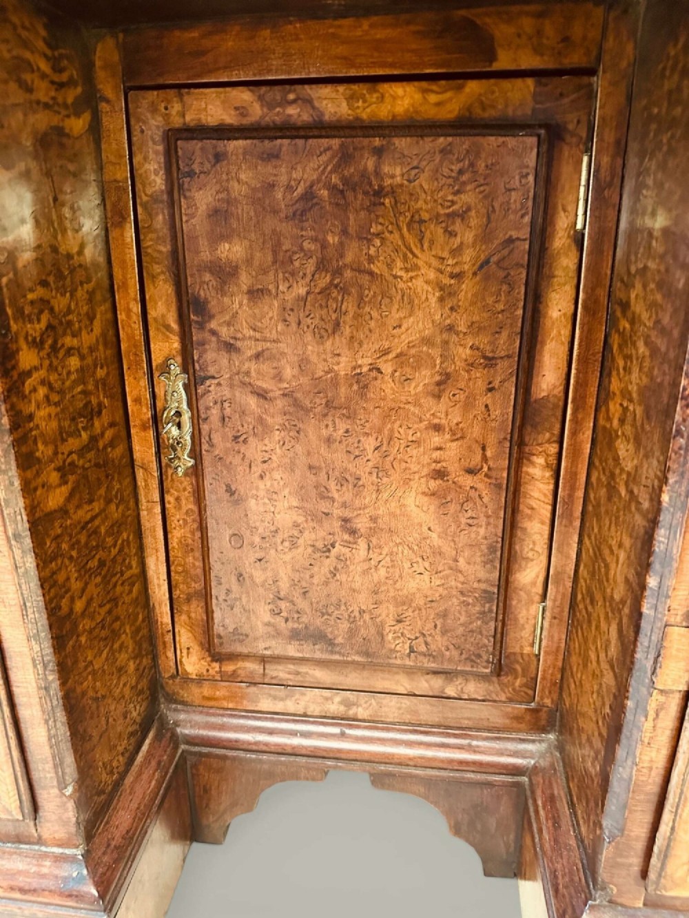 An antique Georgian kneehole bureau in warm brown burr oak featuring multiple small drawers, brass drop handles, a central cupboard, and a hinged top surface. View XI