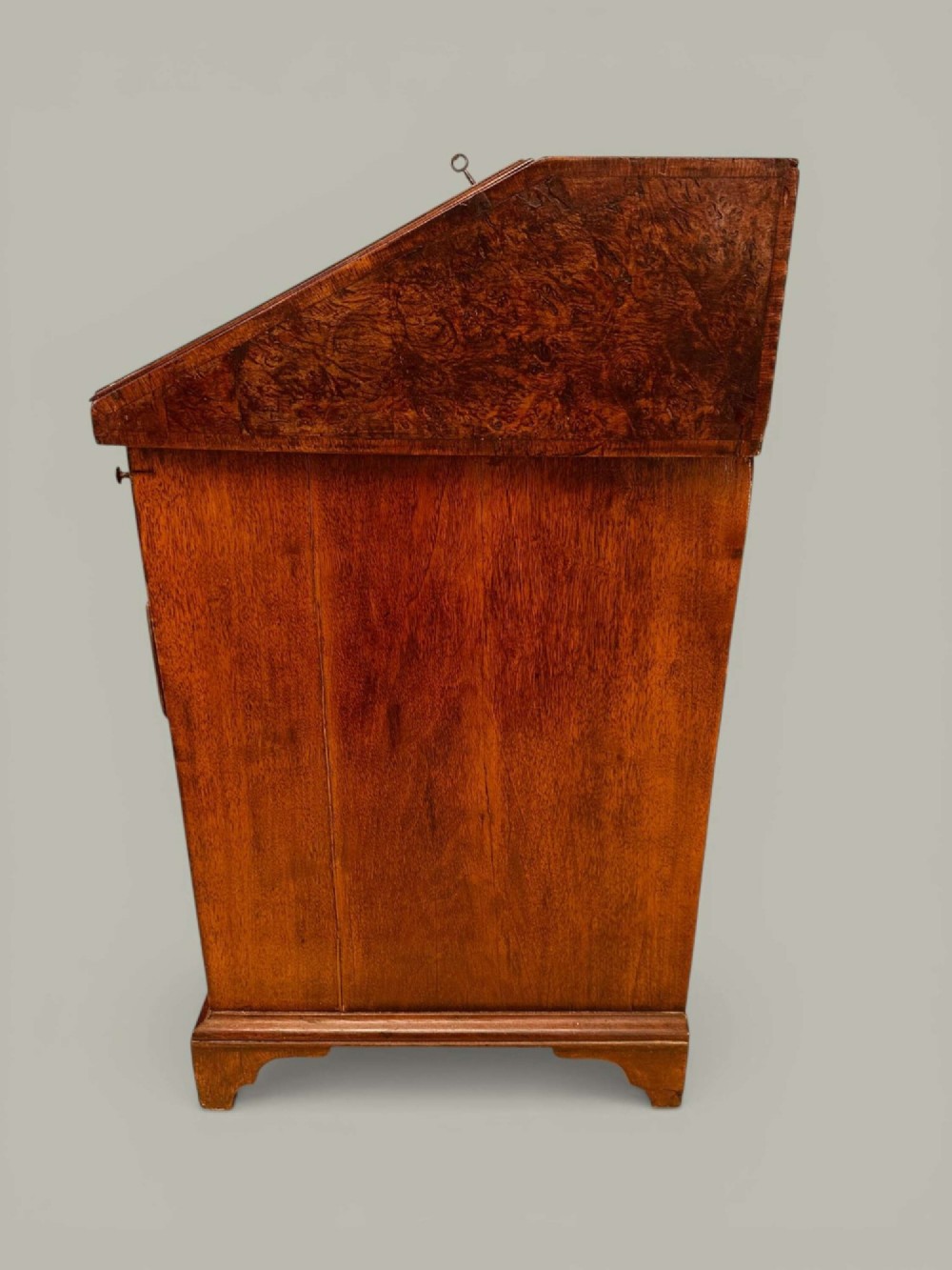 An antique Georgian kneehole bureau in warm brown burr oak featuring multiple small drawers, brass drop handles, a central cupboard, and a hinged top surface. View XIII