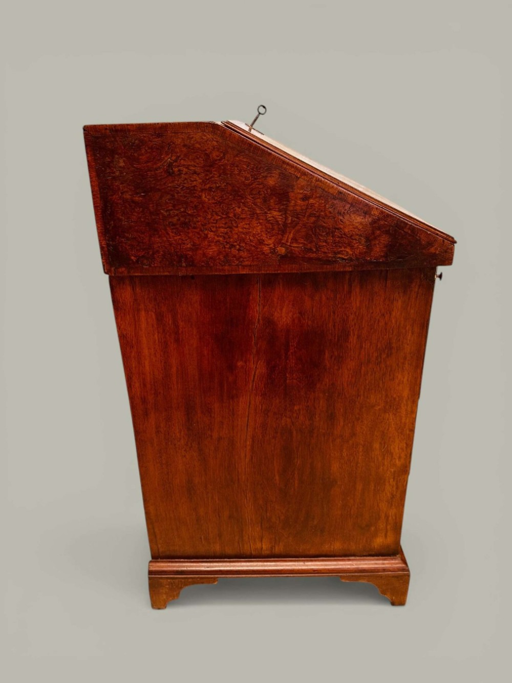 An antique Georgian kneehole bureau in warm brown burr oak featuring multiple small drawers, brass drop handles, a central cupboard, and a hinged top surface. View XIV