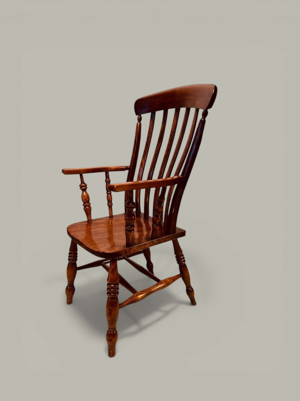 A late nineteenth-century wooden Windsor armchair featuring a curved slat back rest, turned legs, an H-stretcher, and shaped armrests finished in warm brown timber tones.
