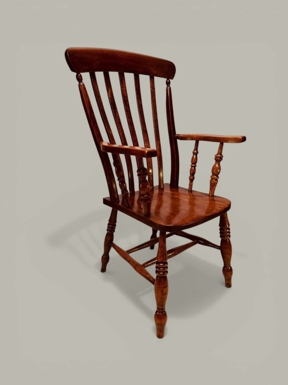 A late nineteenth-century wooden Windsor armchair featuring a curved slat back rest, turned legs, an H-stretcher, and shaped armrests finished in warm brown timber tones. View II