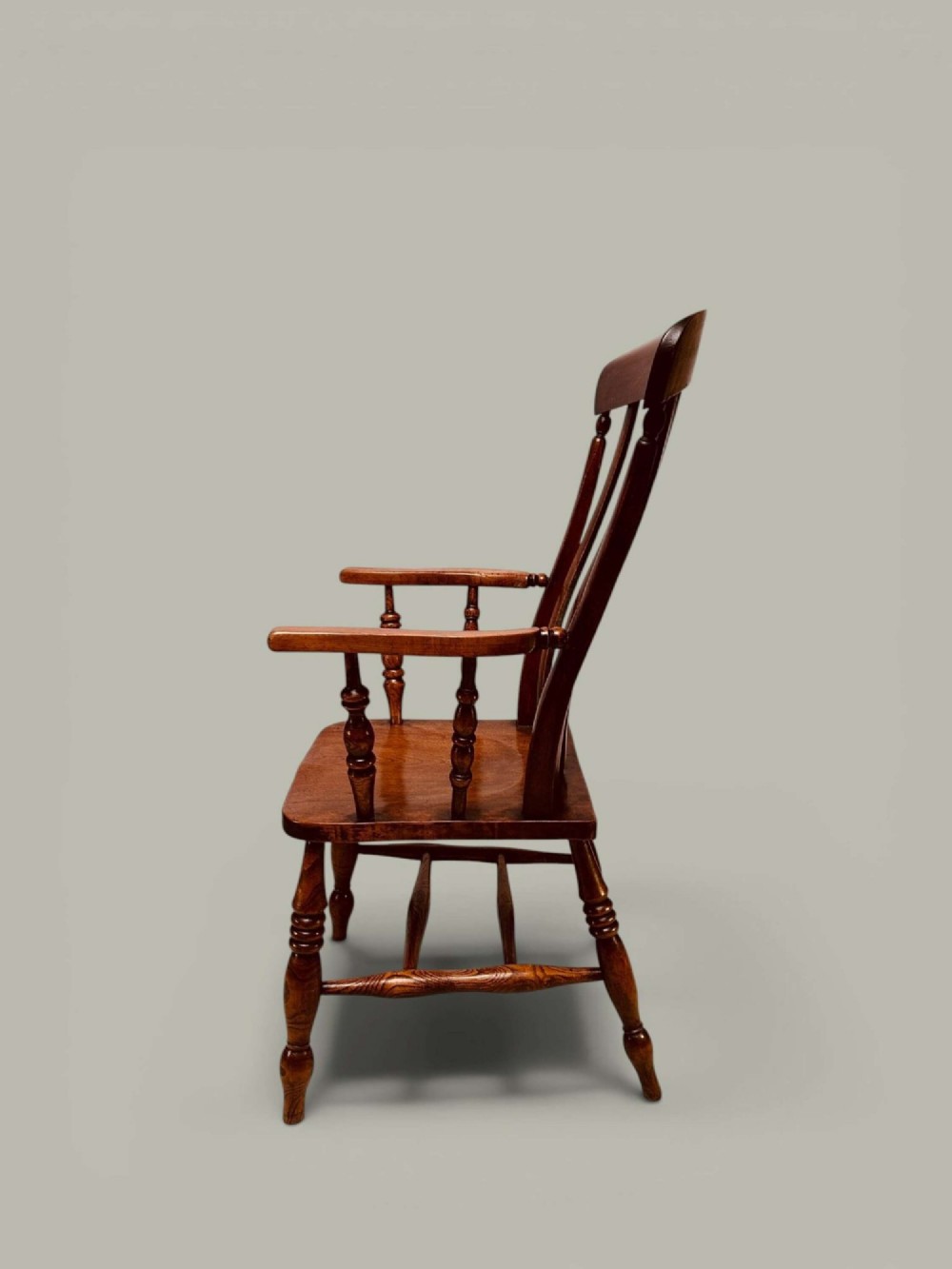 A late nineteenth-century wooden Windsor armchair featuring a curved slat back rest, turned legs, an H-stretcher, and shaped armrests finished in warm brown timber tones. View IV
