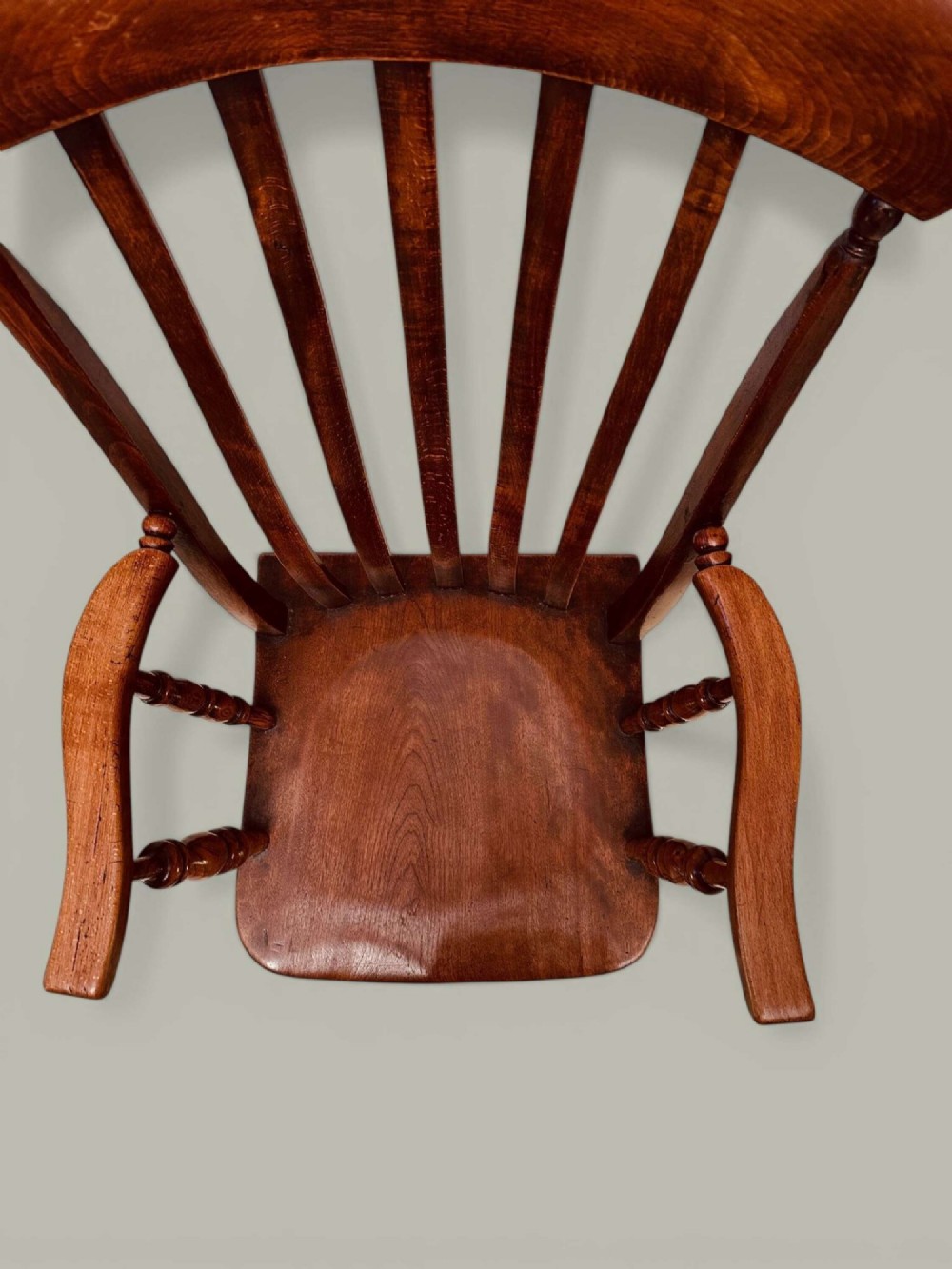 A late nineteenth-century wooden Windsor armchair featuring a curved slat back rest, turned legs, an H-stretcher, and shaped armrests finished in warm brown timber tones. View V