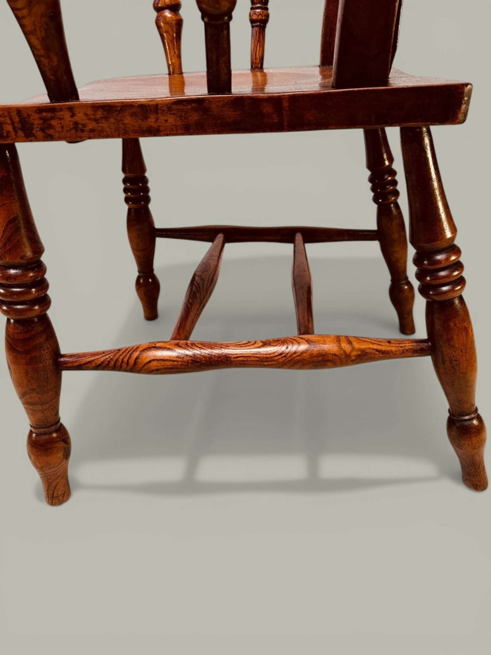 A late nineteenth-century wooden Windsor armchair featuring a curved slat back rest, turned legs, an H-stretcher, and shaped armrests finished in warm brown timber tones. View VI