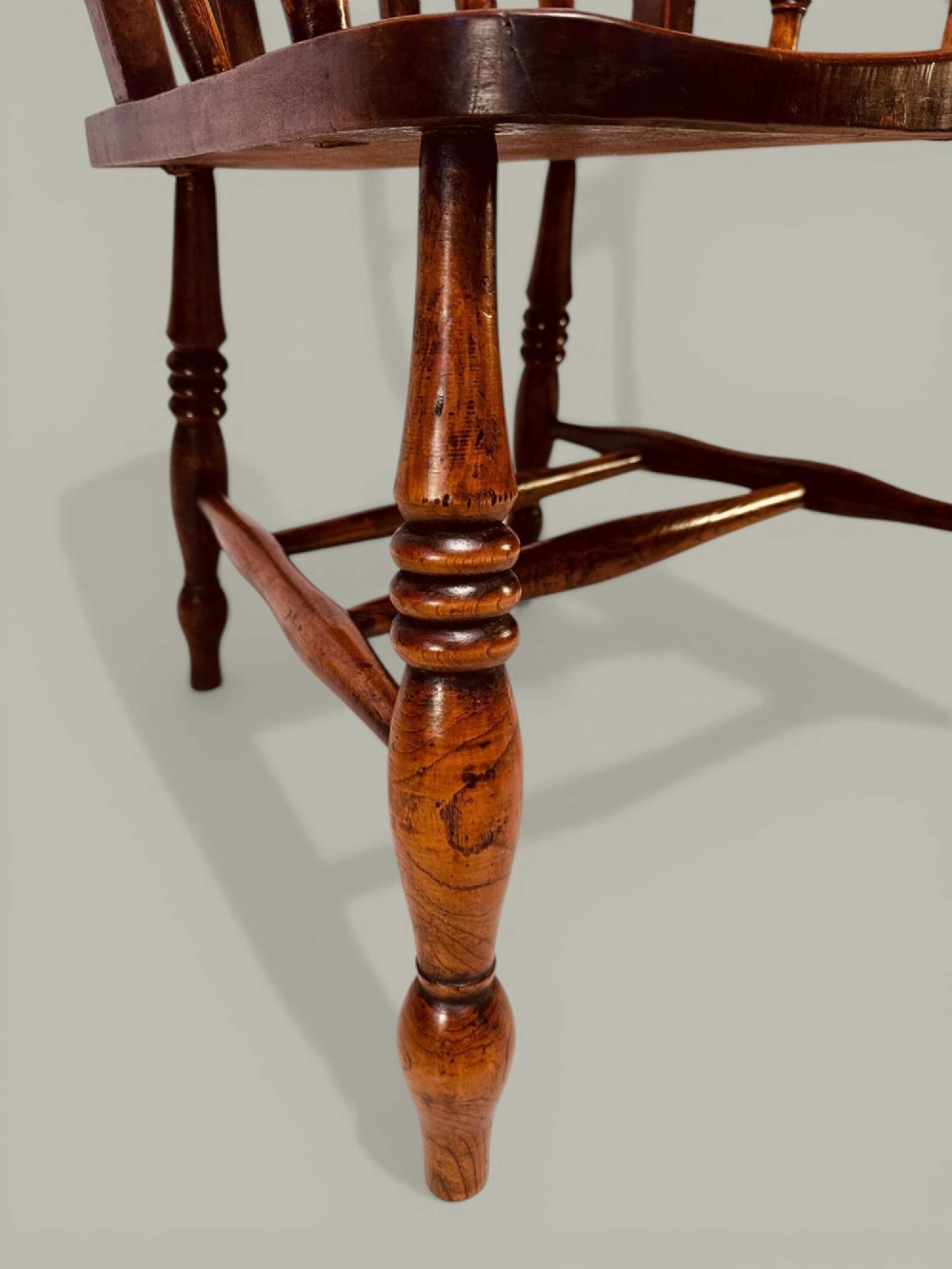A late nineteenth-century wooden Windsor armchair featuring a curved slat back rest, turned legs, an H-stretcher, and shaped armrests finished in warm brown timber tones. View IX