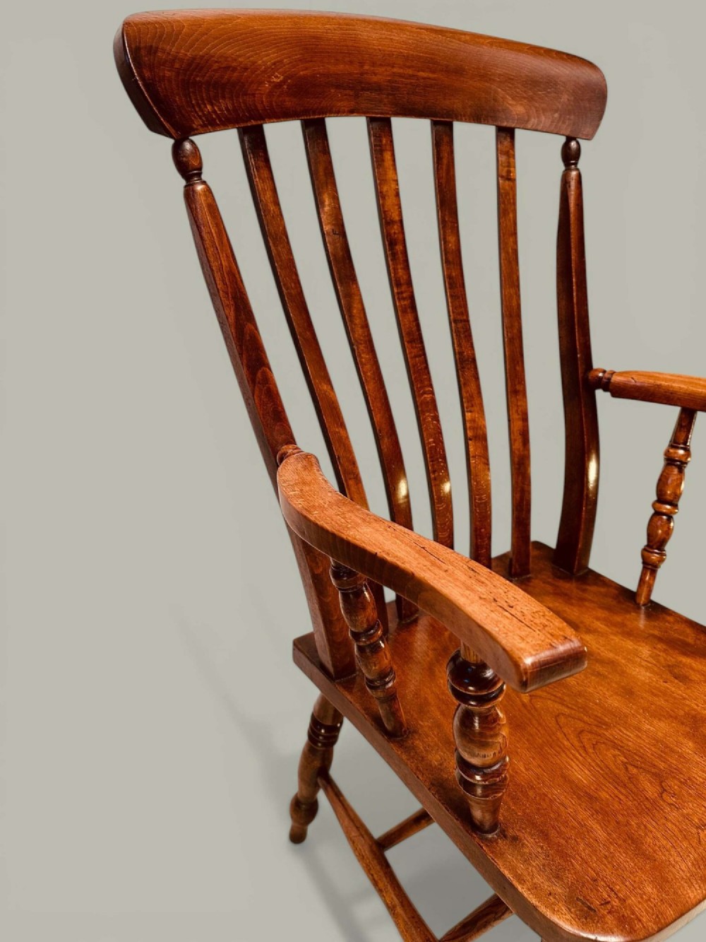 A late nineteenth-century wooden Windsor armchair featuring a curved slat back rest, turned legs, an H-stretcher, and shaped armrests finished in warm brown timber tones. View XI