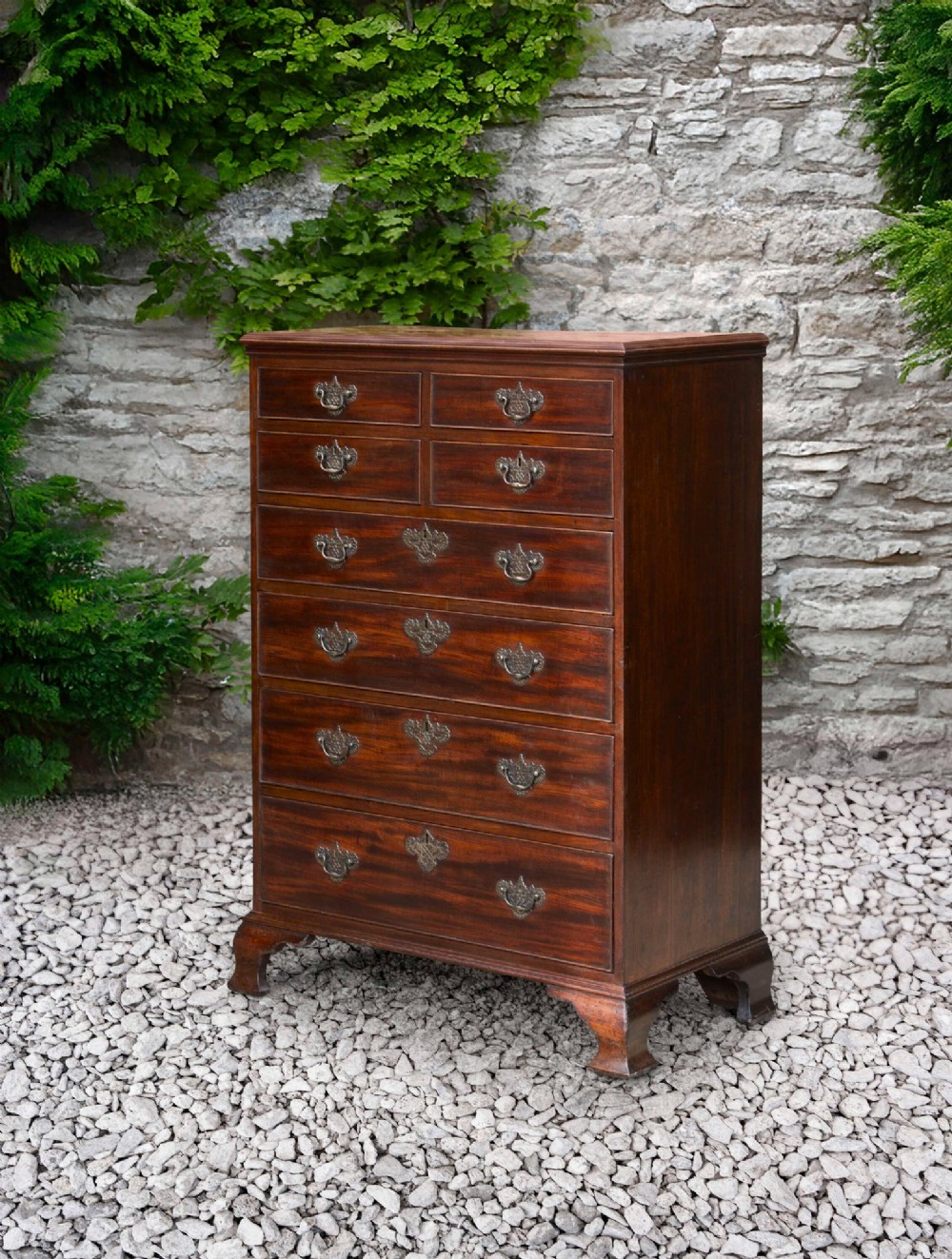 An eighteenth-century Georgian mahogany tall chest of drawers featuring brass handles, keyhole escutcheons, and ogee bracket feet.