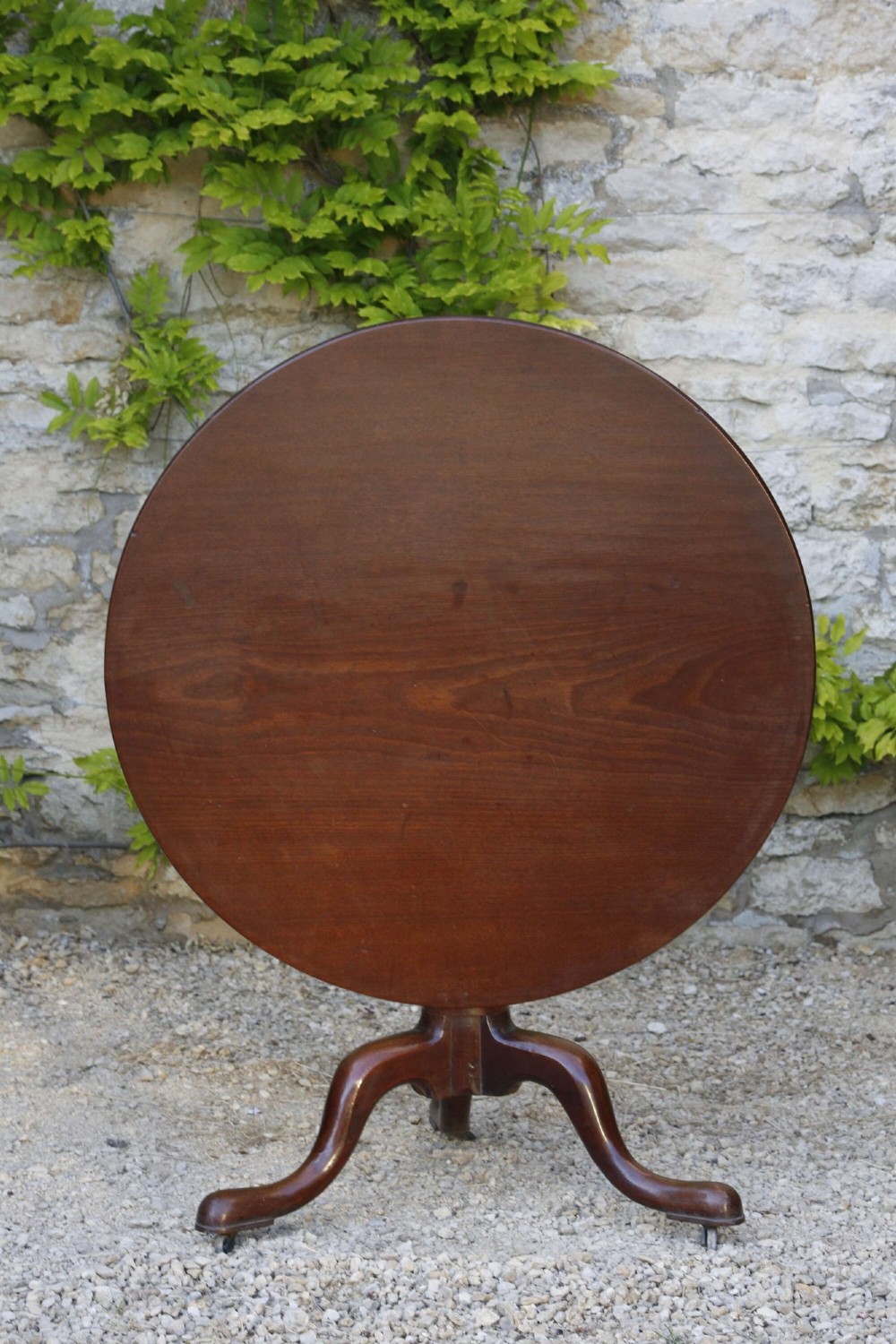 An 18th-century George III mahogany tilt-top table with a circular top raised vertically on a turned stem and splayed tripod cabriole legs.