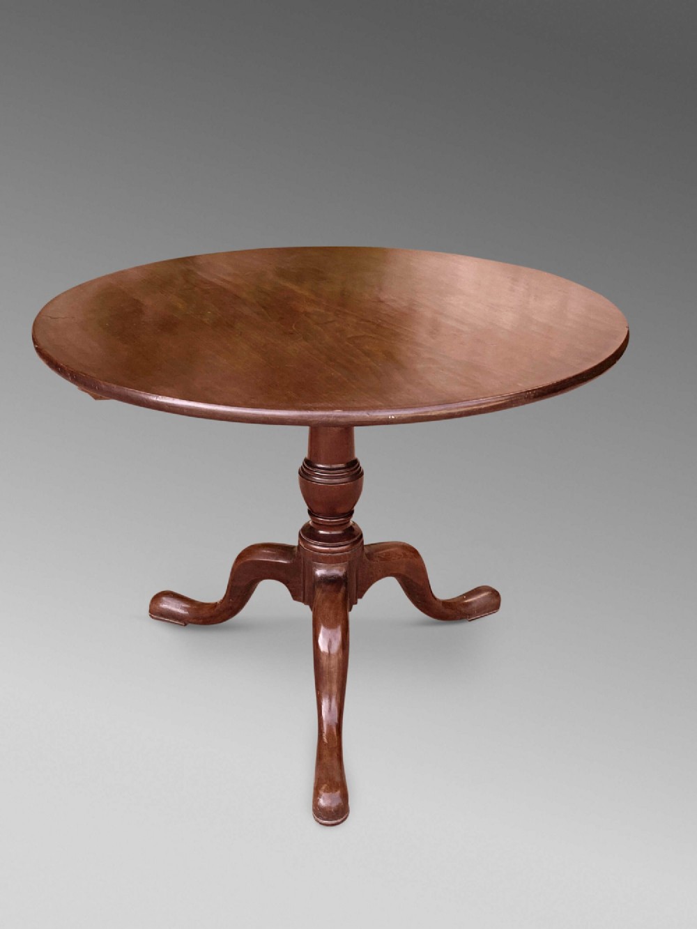 An 18th-century George III mahogany tilt-top table with a circular top raised vertically on a turned stem and splayed tripod cabriole legs. View II