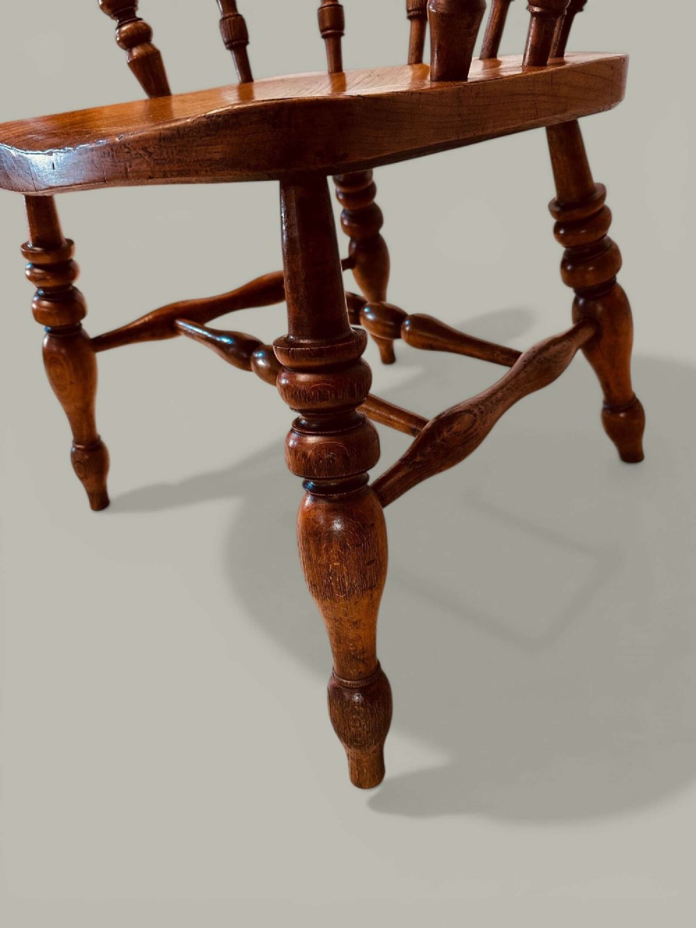 A low-backed wooden Windsor armchair crafted from ash and elm with turned spindles, a curved horseshoe armrest, and a shaped saddle seat. View X