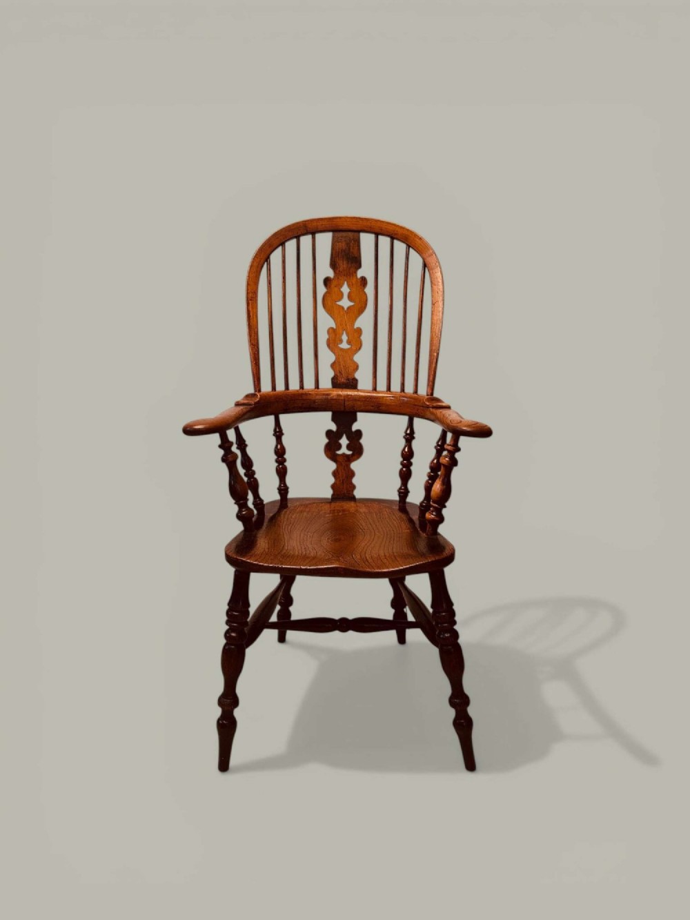 A late nineteenth-century Windsor armchair crafted from ash and elm with a hoop back, decorative pierced splat, broad armrests, and turned legs.