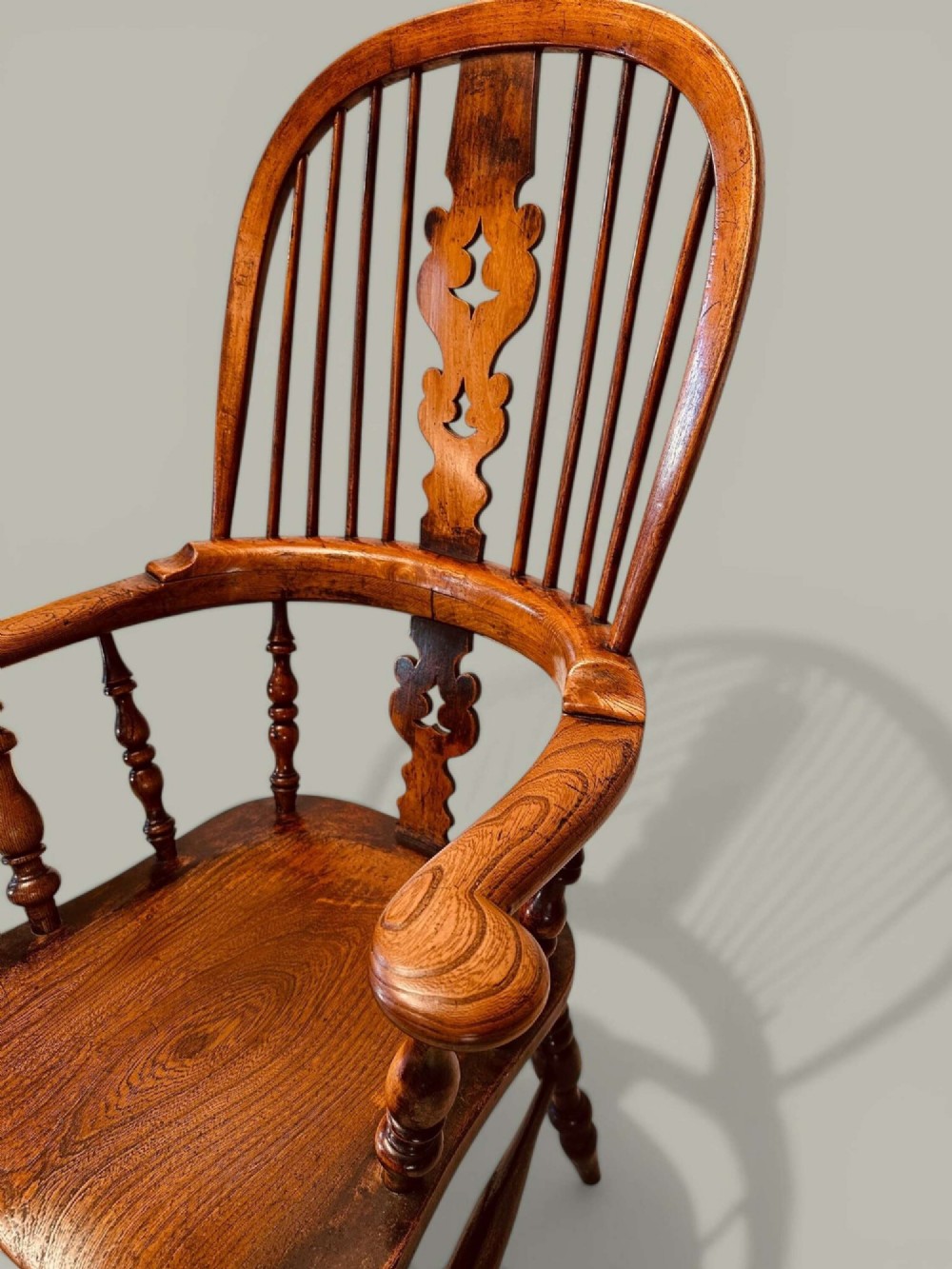A late nineteenth-century Windsor armchair crafted from ash and elm with a hoop back, decorative pierced splat, broad armrests, and turned legs. View X