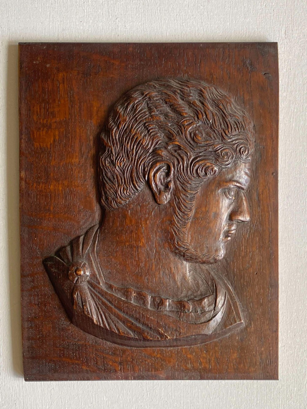 A rectangular dark oak panel featuring a high-relief carving of a Roman emperor profile in profile view. View II