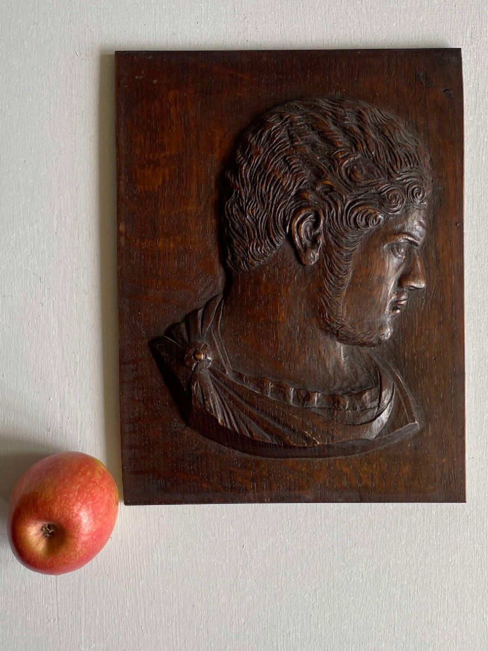 A rectangular dark oak panel featuring a high-relief carving of a Roman emperor profile in profile view. View IV
