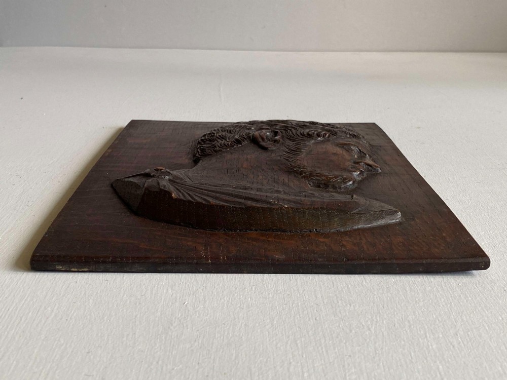 A rectangular dark oak panel featuring a high-relief carving of a Roman emperor profile in profile view. View V