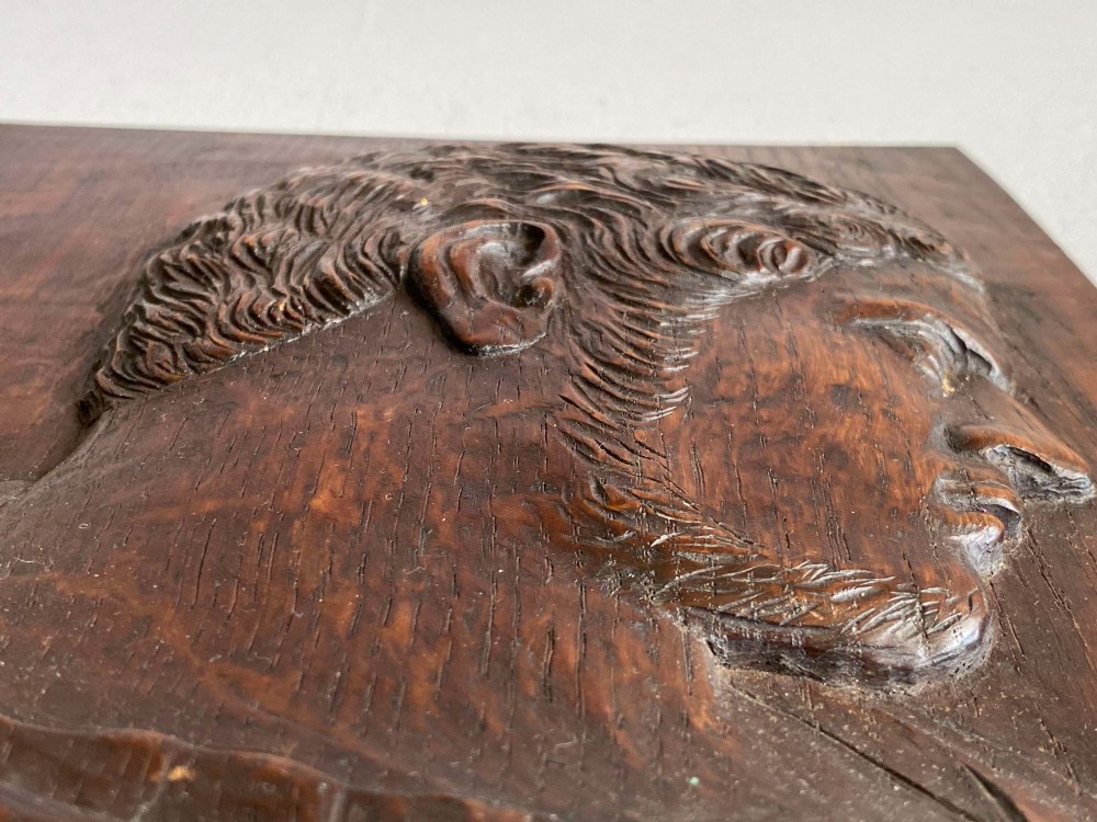 A rectangular dark oak panel featuring a high-relief carving of a Roman emperor profile in profile view. View VII