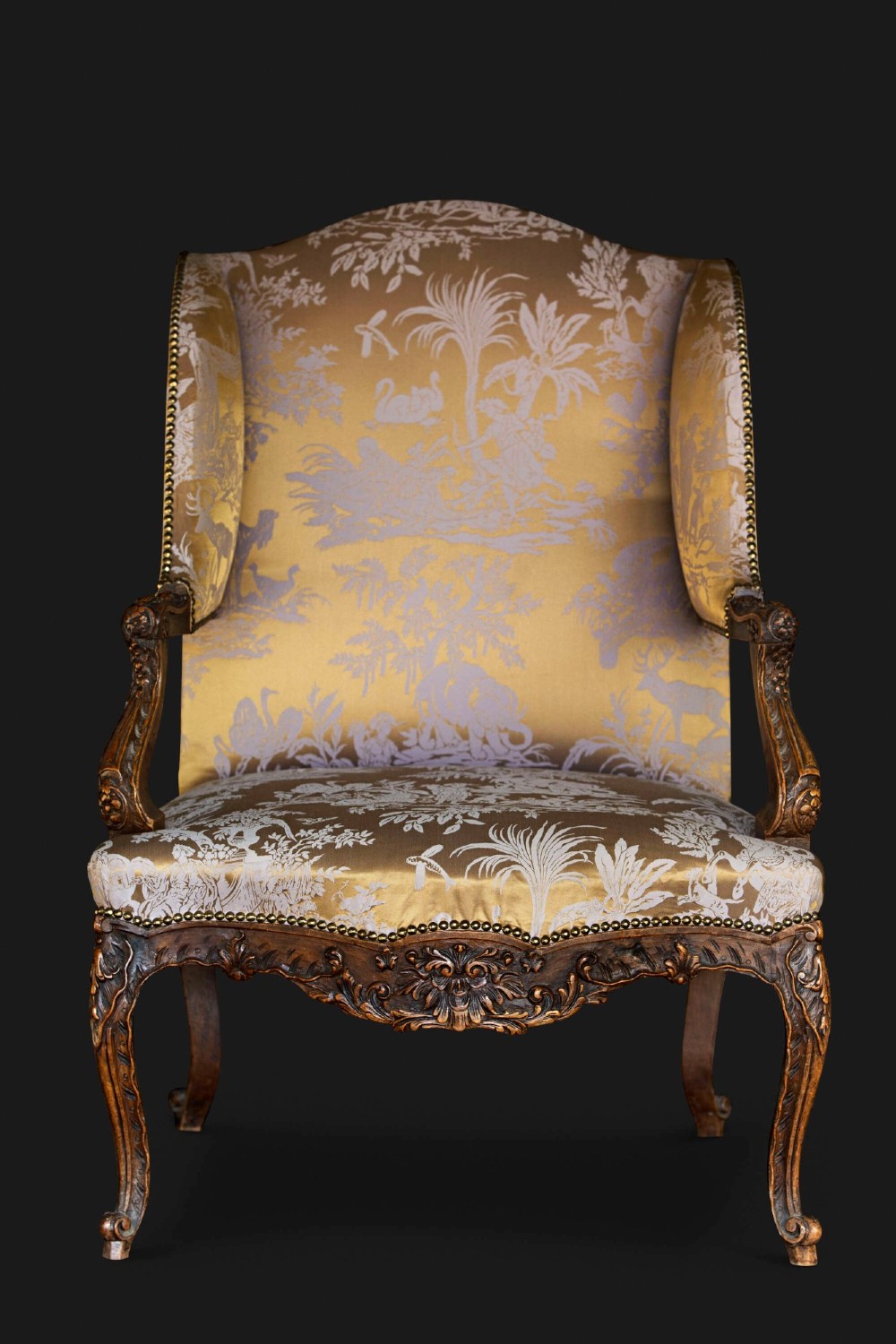 A 19th-century French Louis XV style wingback armchair with carved wood framing, cabriole legs, and gold pattern damask upholstery.