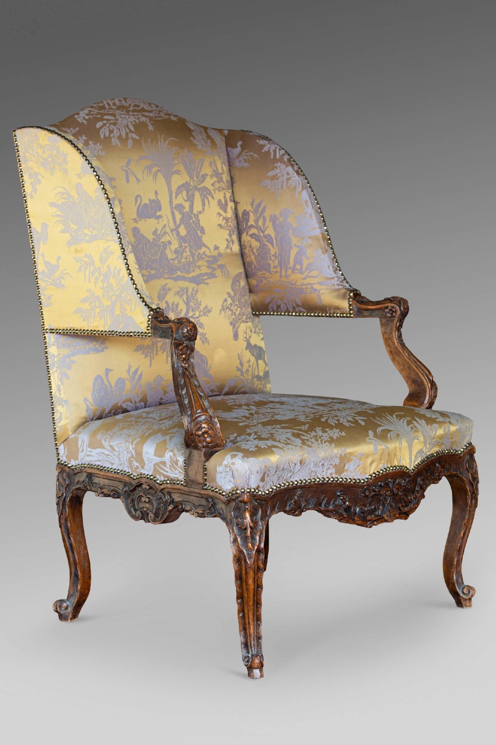A 19th-century French Louis XV style wingback armchair with carved wood framing, cabriole legs, and gold pattern damask upholstery. View X