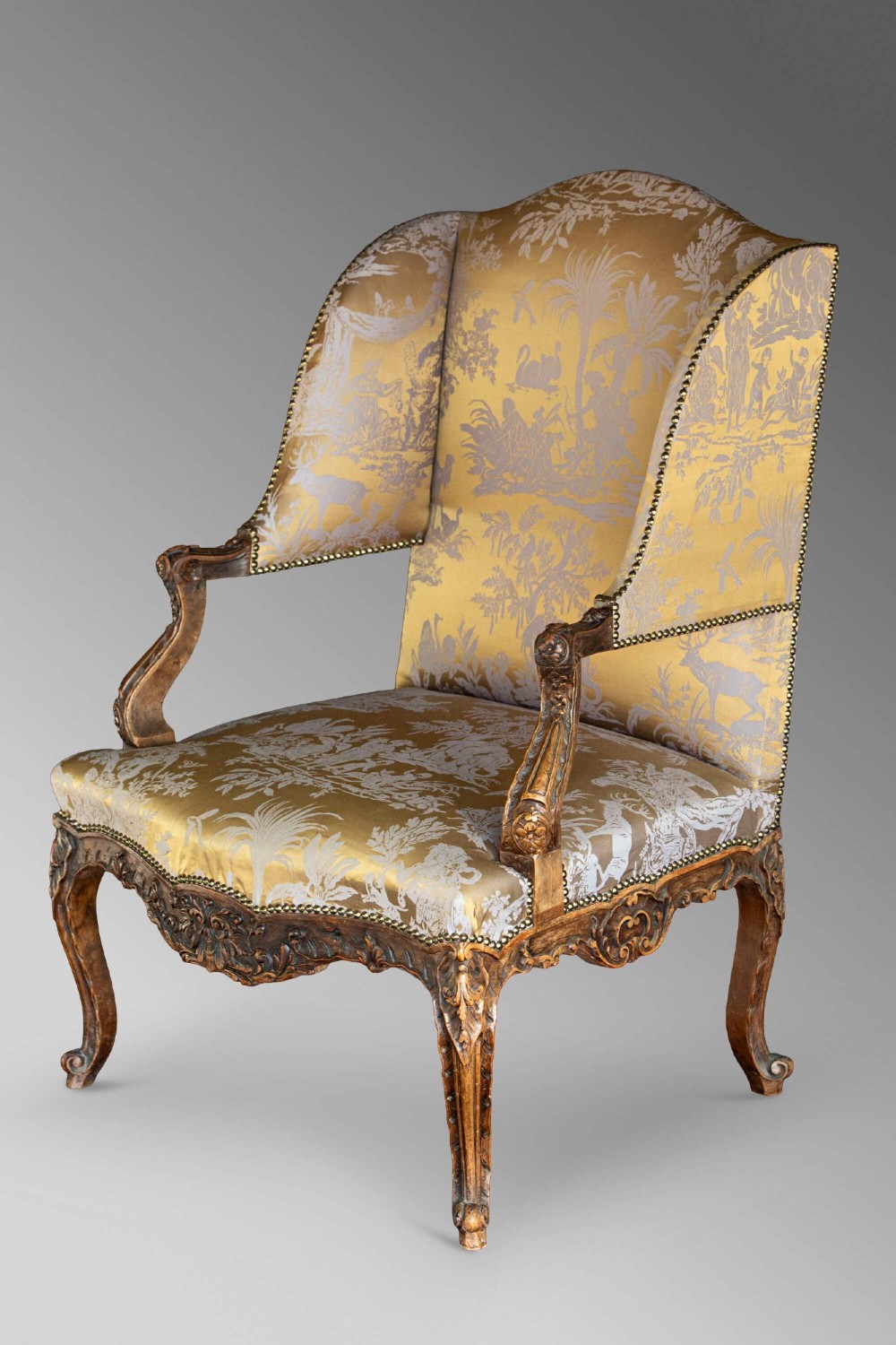 A 19th-century French Louis XV style wingback armchair with carved wood framing, cabriole legs, and gold pattern damask upholstery. View XV