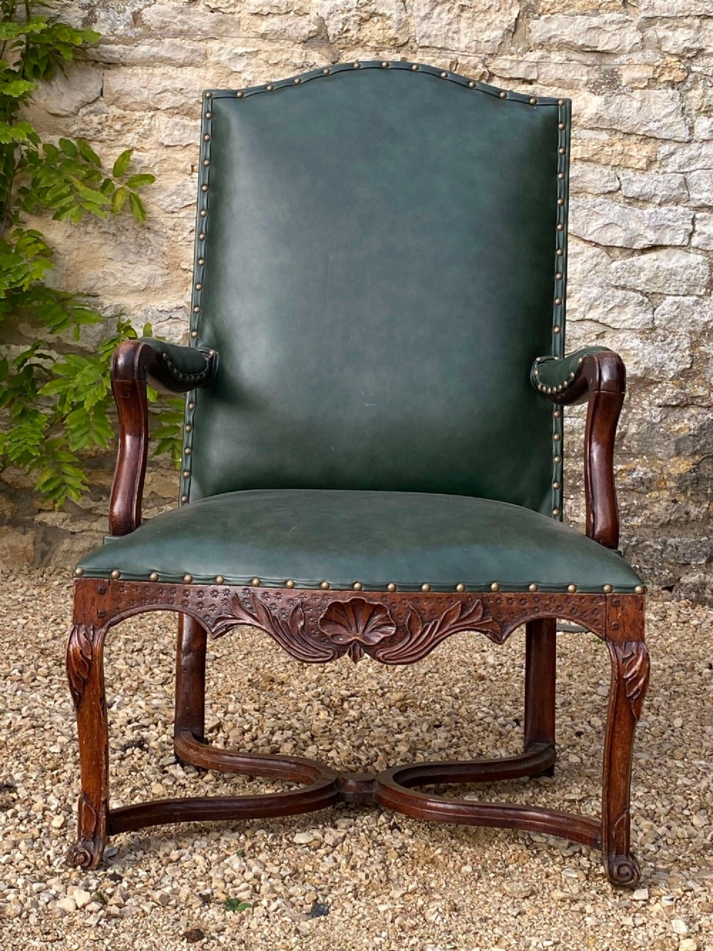 An eighteenth-century French walnut fauteuil armchair upholstered in dark green leather with brass studding, carved apron details, and curved legs. View II