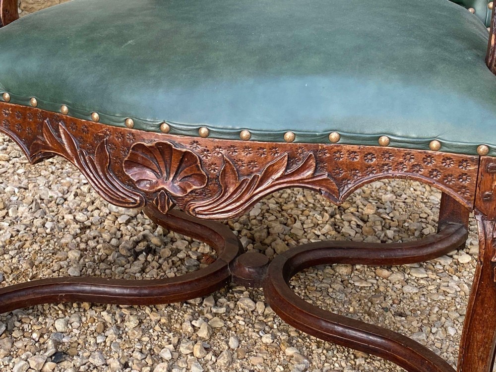 An eighteenth-century French walnut fauteuil armchair upholstered in dark green leather with brass studding, carved apron details, and curved legs. View V