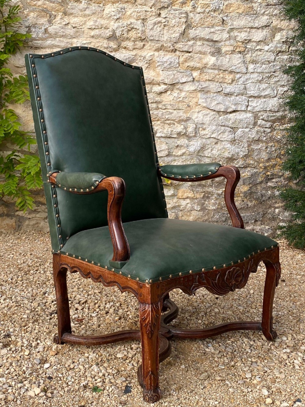 An eighteenth-century French walnut fauteuil armchair upholstered in dark green leather with brass studding, carved apron details, and curved legs. View VI