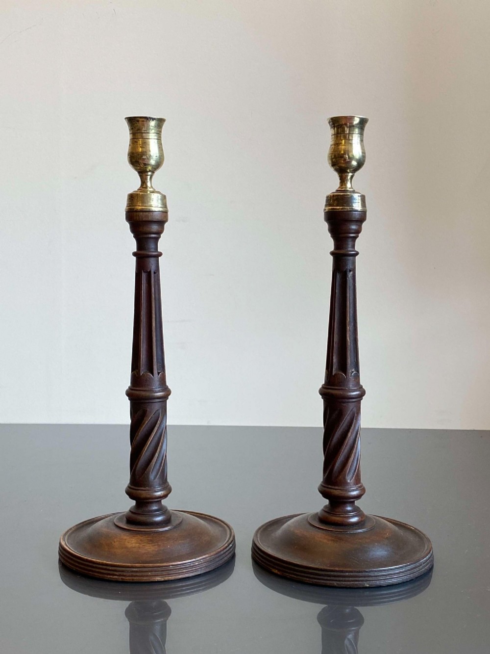 A pair of turned dark mahogany candlesticks featuring fluted and spiral columns topped with brass nozzles on circular bases.