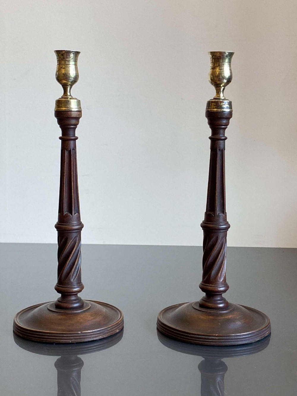 A pair of turned dark mahogany candlesticks featuring fluted and spiral columns topped with brass nozzles on circular bases. View VII