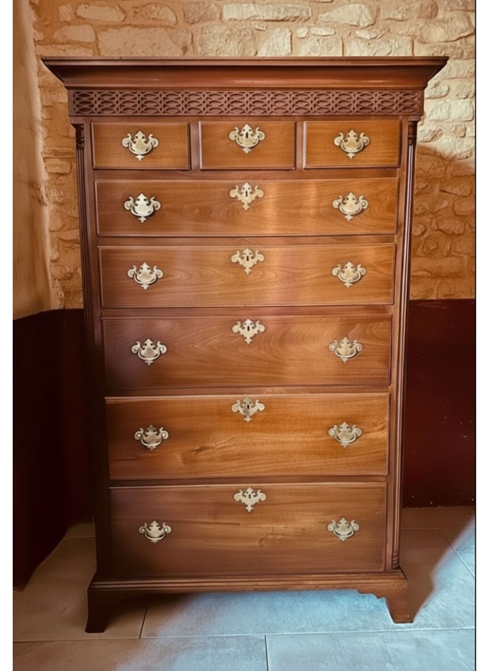 A tall 19th-century walnut chest of drawers featuring a carved fretwork frieze, brass backplate handles, and graduated drawer fronts.