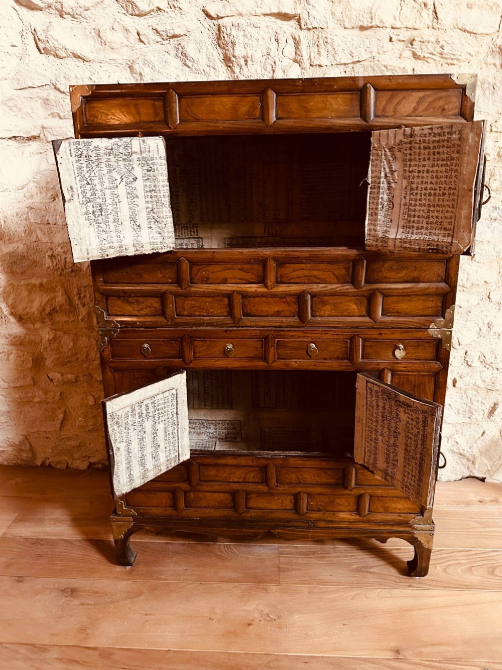A two-tier Korean elm cabinet with intricate brass corner plates, decorative lock fittings, panelled doors, and red drop tassels. View V