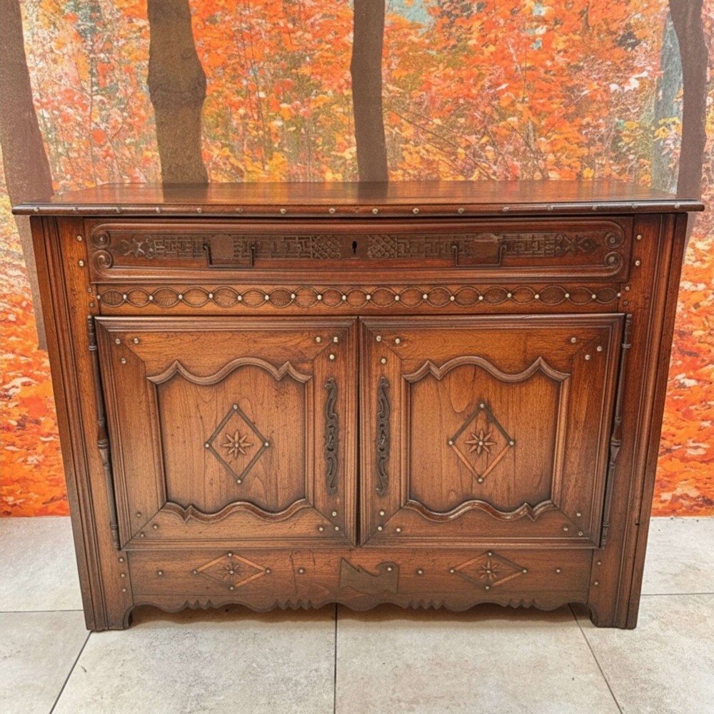 An antique French chestnut buffet featuring a carved top drawer band, two moulded door panels with carved star motifs, and iron hardware.