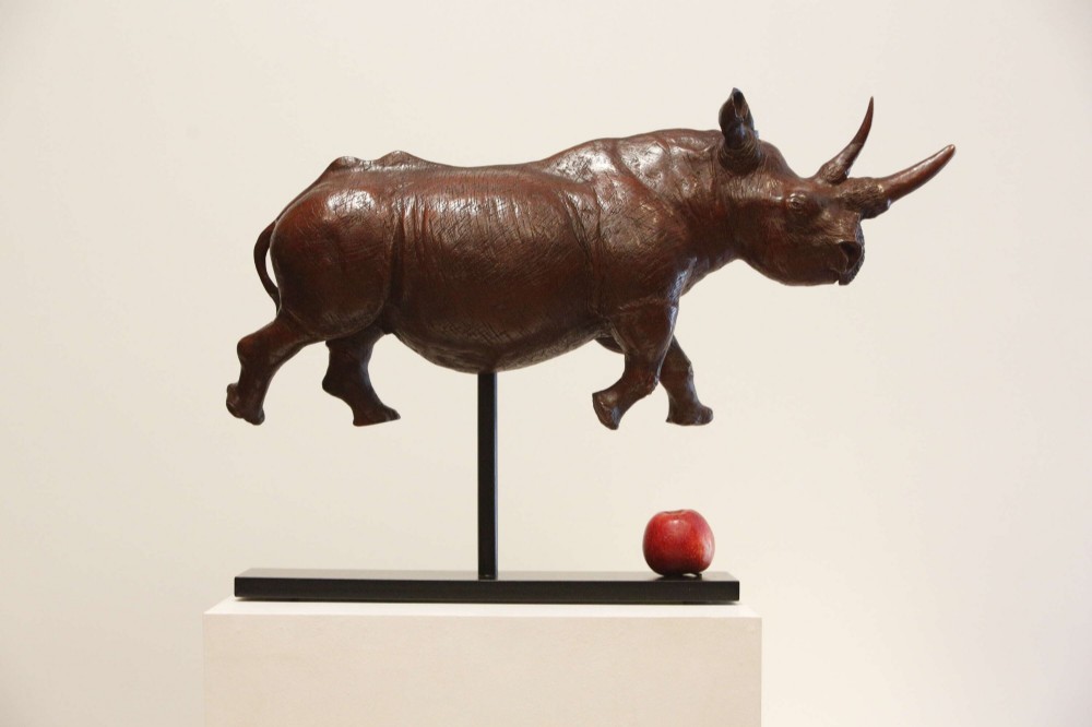 A carved reddish-brown ironwood sculpture of a rhinoceros mounted on a black metal display stand.