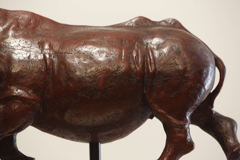 A carved reddish-brown ironwood sculpture of a rhinoceros mounted on a black metal display stand. View III