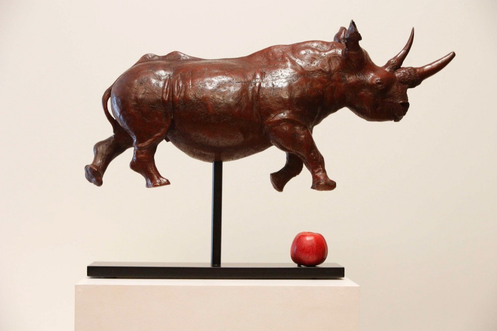 A carved reddish-brown ironwood sculpture of a rhinoceros mounted on a black metal display stand. View IV